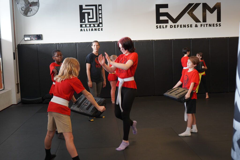 Children practicing self defense drills with strike shields during EVKM kids class in Tempe